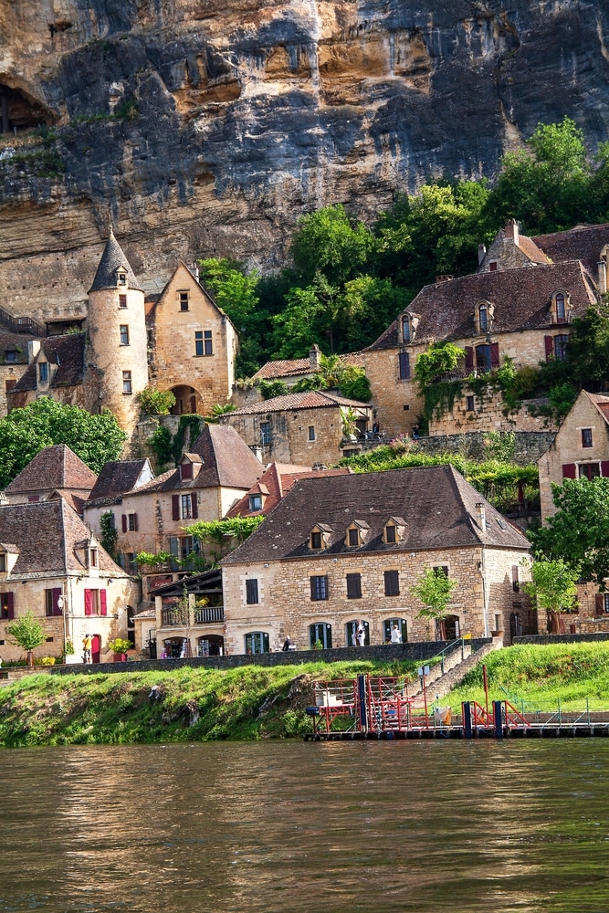 Village de La Roque-Gageac en Dordogne : Panorama Fluvial Village médiéval de La Roque-Gageac avec maisons en pierre nichées sous une falaise au bord de la Dordogne.