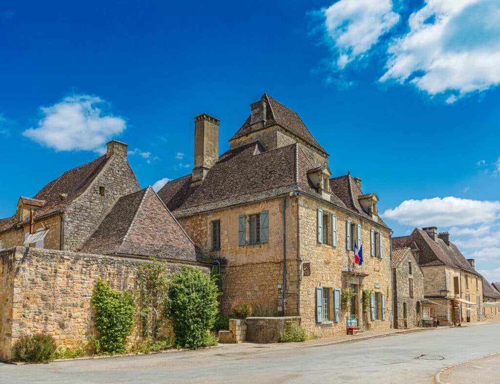 Charme d'un village médiéval en pierre sous le soleil Charming street scene of a historic French village with stone buildings under a blue sky.